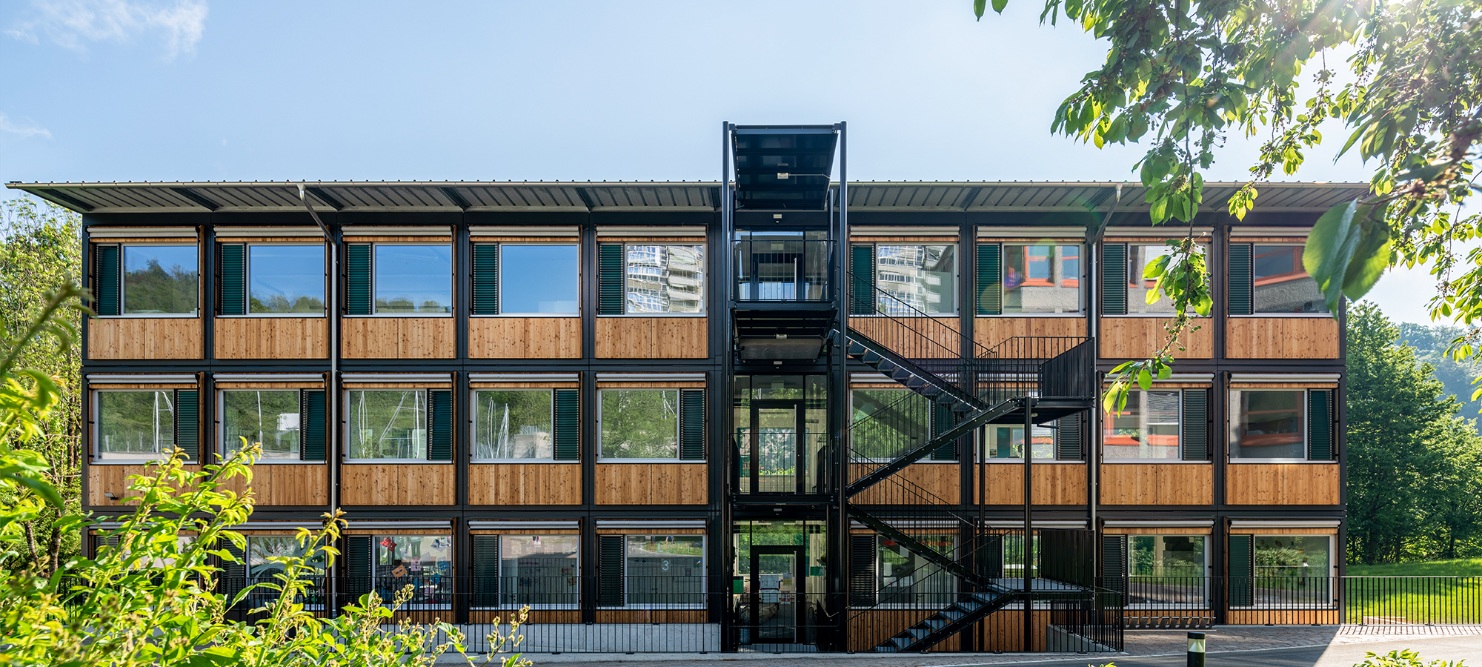 Gesamtansicht des ZM10-Schulpavillons Sihlweid in Zürich frontal von vorne, mit Pflanzen im Vordergrund