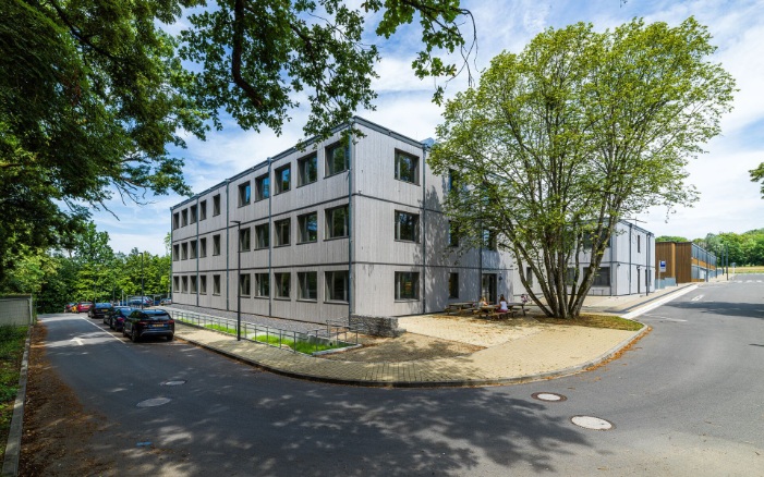 Graue Fassade des Schulmodulbaus mit vertikalen Holzleisten