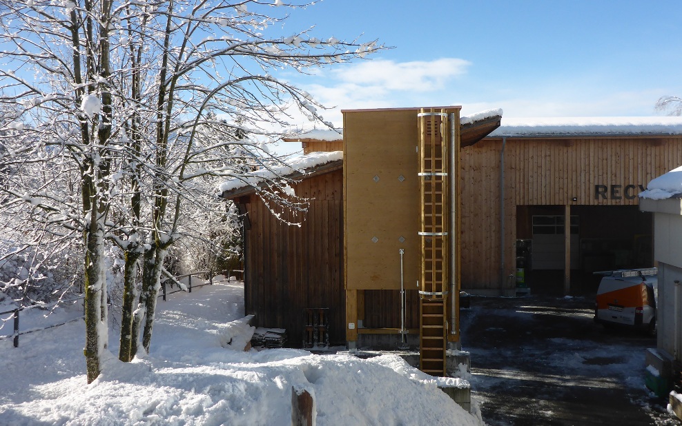 Silo carré (E4) en bois de 30 m³ avec échelle en bois accolé à un bâtiment en bois dans un paysage hivernal